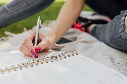 Crop female noting down daily plans in notebook in park